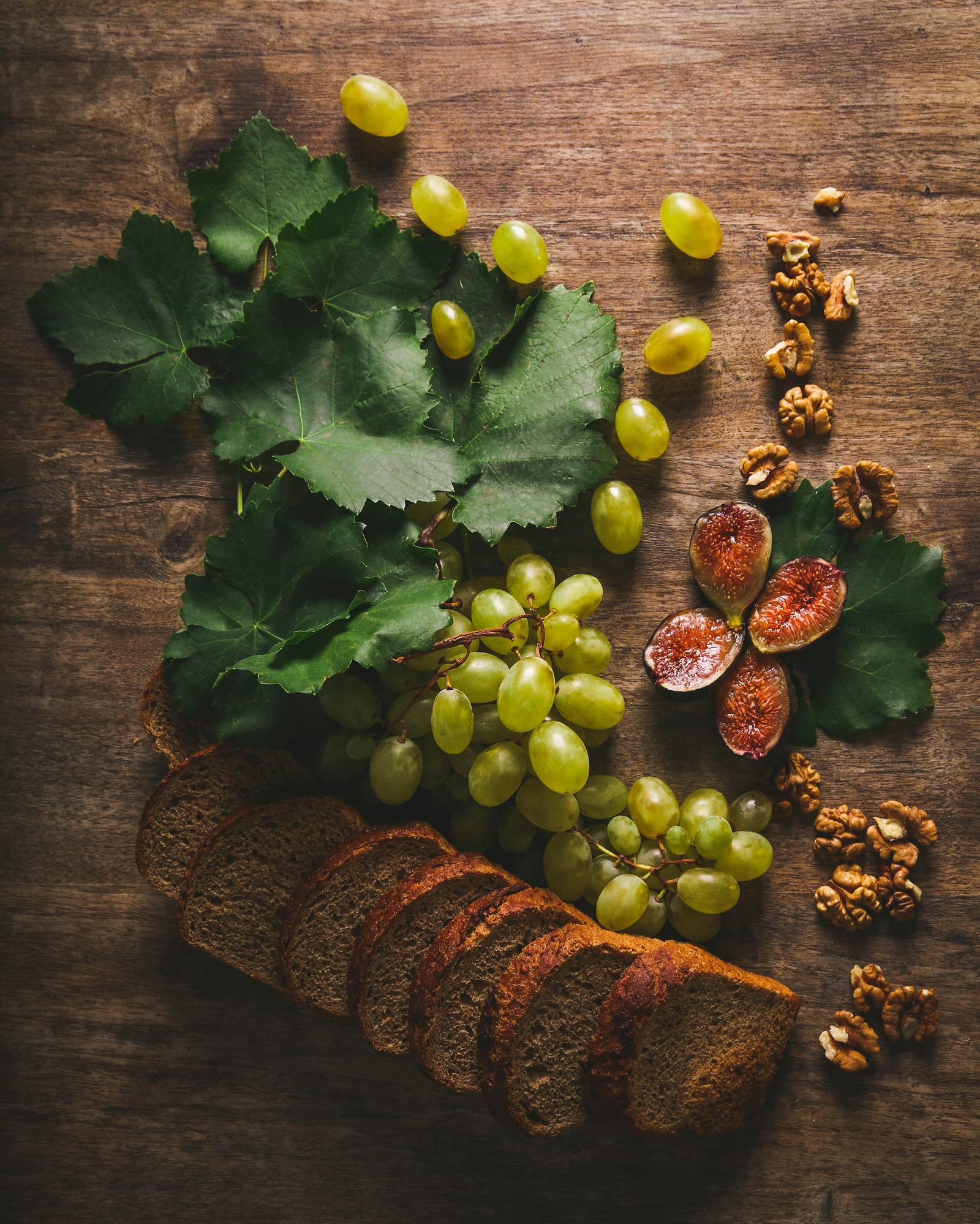 Rustic still life of grapes, sliced bread, figs, and walnuts on wooden table.